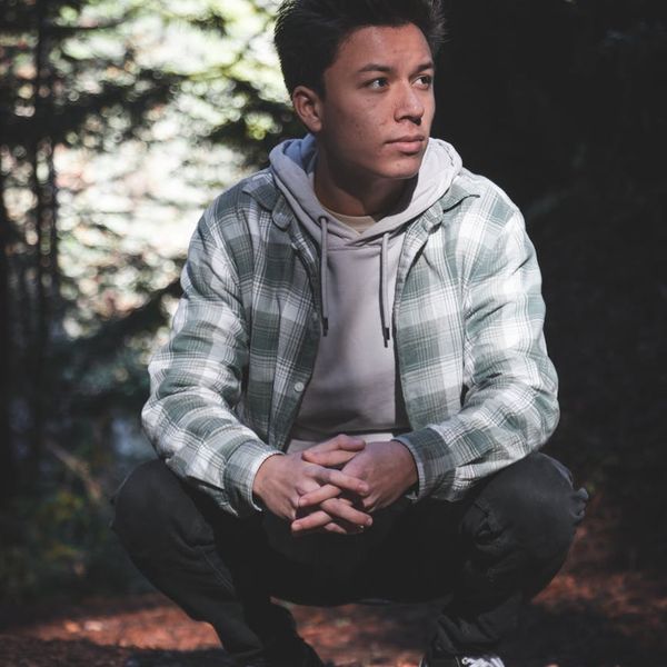 Person meditating outdoors with a serene natural background of trees and sunlight.